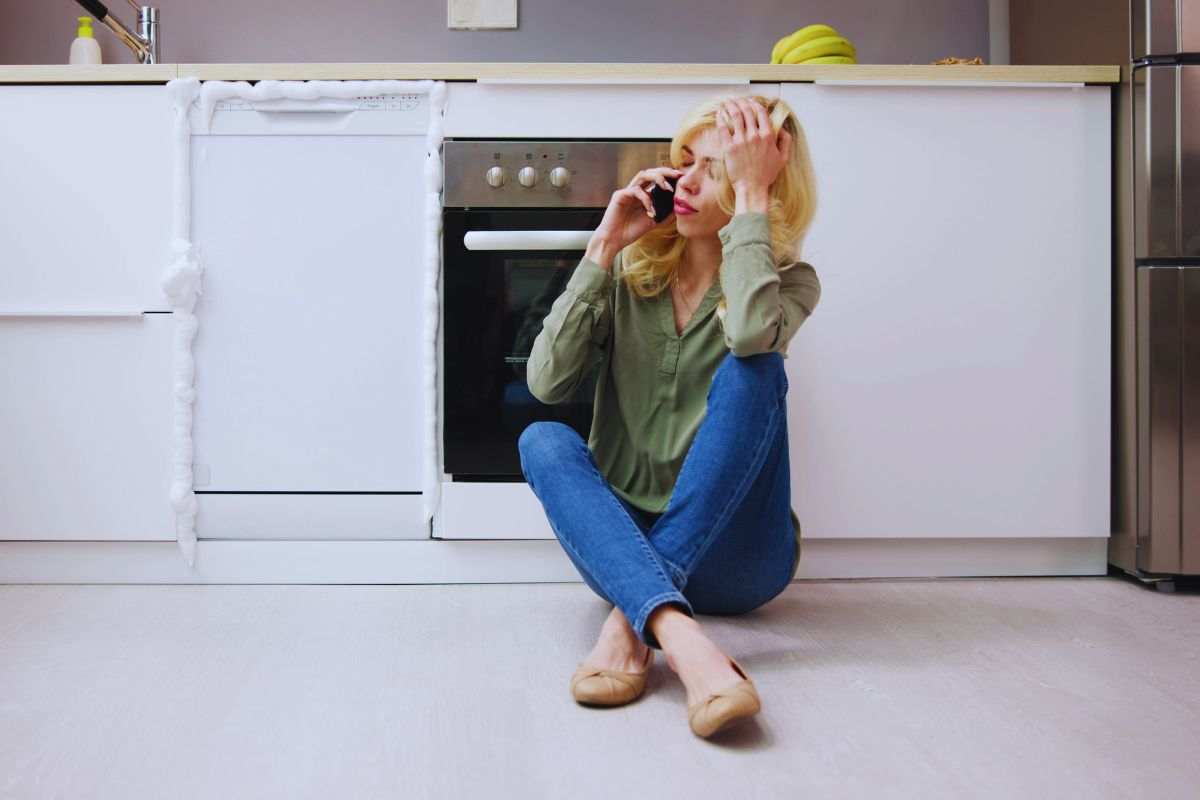 Donna seduta per terra che chiama tecnico lavastoviglie